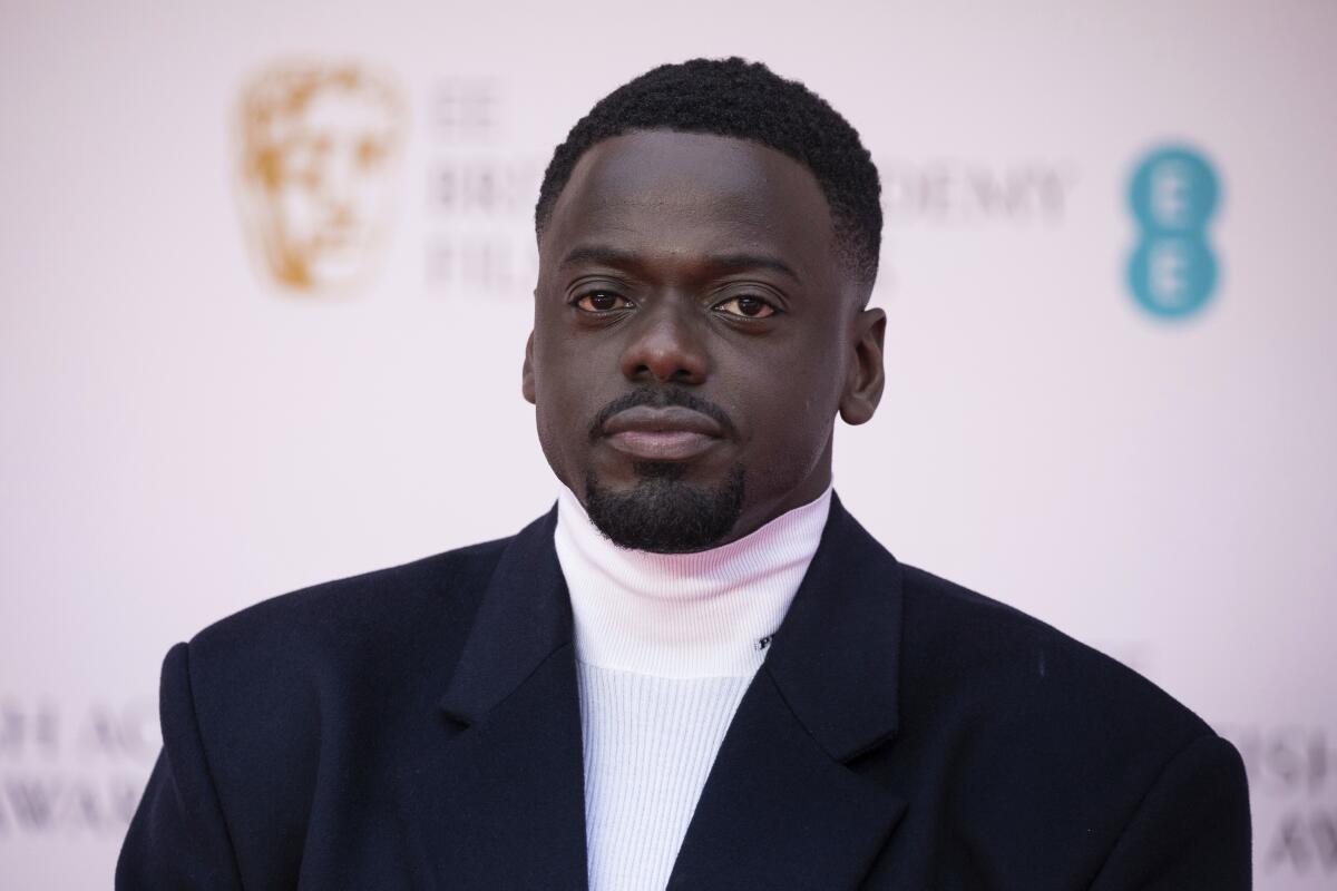 A man in a dark suit and white turtleneck.