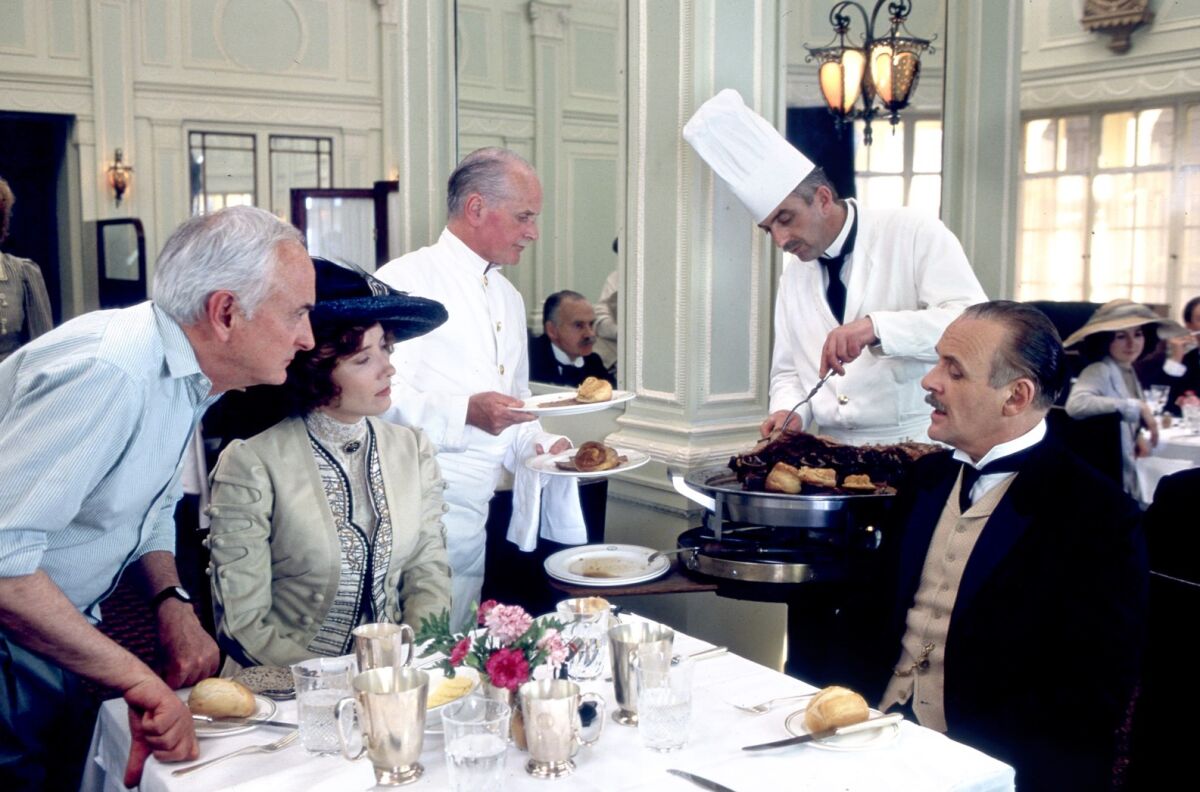  James Ivory leans on a restaurant table where actors Emma Thompson and Anthony Hopkins sit in period costume 
