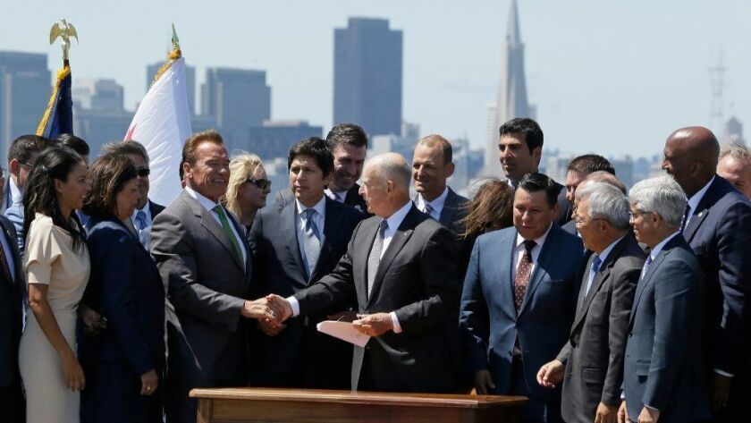 Arnold Schwarzenegger, alongside Kevin de León, shakes hands with then-Gov. Jerry Brown at a 2017 event for legislation aimed at reducing climate change.