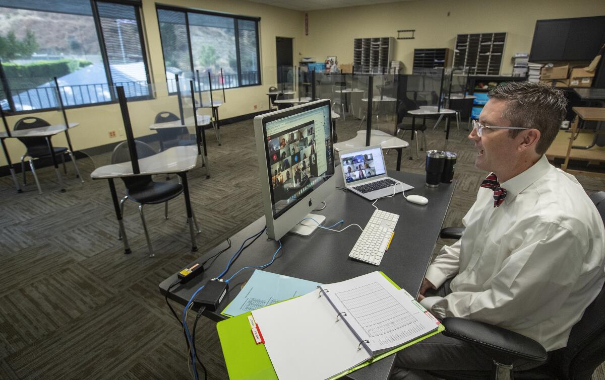 A man at a desk facing a computer screen, in a classroom.