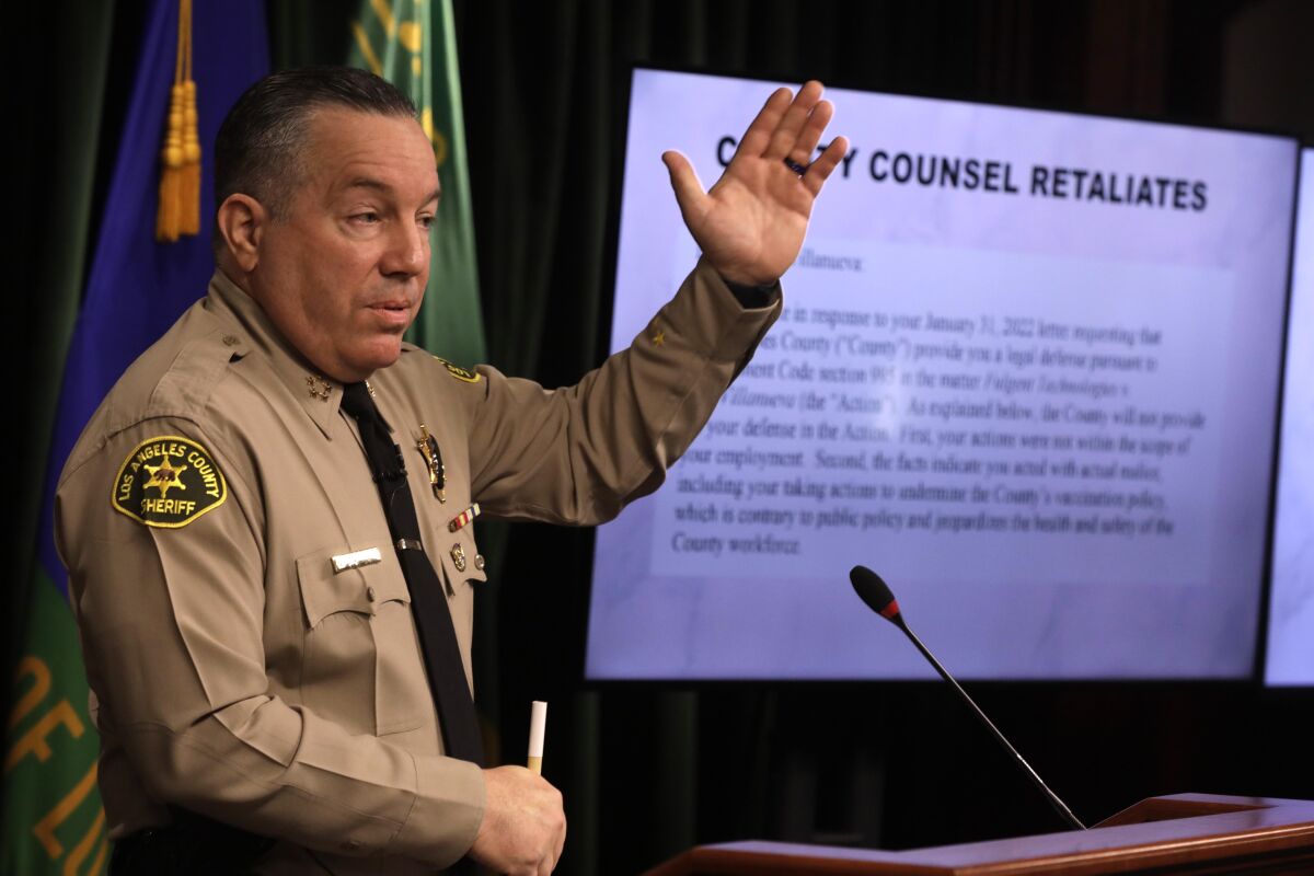 Sheriff Alex Villanueva holds up one hand during a news conference. 