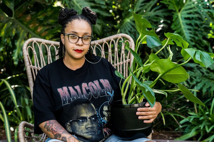 A portrait of Courtney Warwick, seated amid greenery and holding a houseplant.