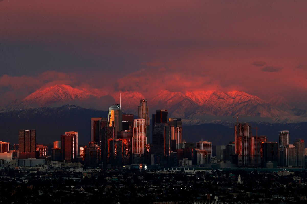The setting sun casts a glow on downtown Los Angeles and the snow-covered San Gabriel Mountains.