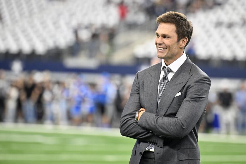 Analyst Tom Brady smiles with folded arms on the field