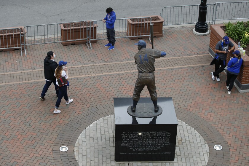 Fans walk by Ernie Banks Statue outside Wrigley Field as a baseball game between the Chicago Cubs and the Los Angels Dodgers was postponed due to the forecast of inclement weather, Monday, May 3, 2021, in Chicago. (AP Photo/Kamil Krzaczynski)
