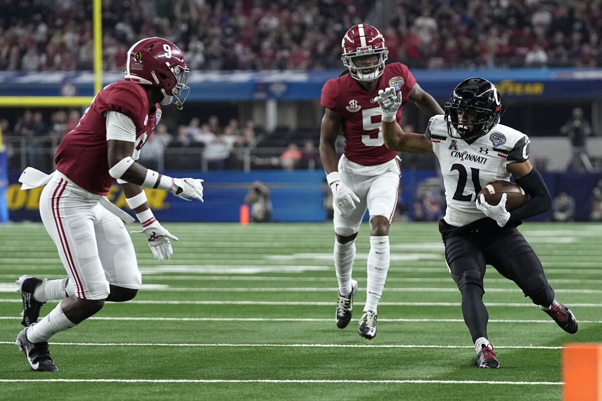 Cincinnati wide receiver Tyler Scott (21) runs for gain after catching a pass as Alabama's Jalyn Armour-Davis (5) and Jordan Battle (9) defend during the first half of the Cotton Bowl NCAA College Football Playoff semifinal game, Friday, Dec. 31, 2021, in Arlington, Texas. (AP Photo/Jeffrey McWhorter)
