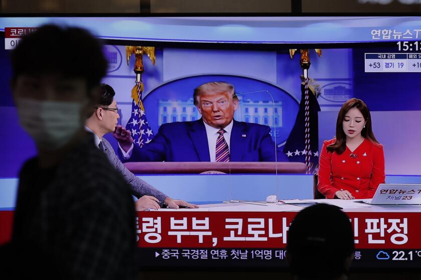 A commuter at the Seoul Railway Station walks past a TV screen featuring coverage about President Trump.