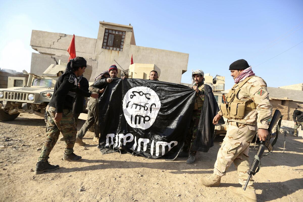 Iraqi army soldiers celebrate as they hold an Islamic State flag.