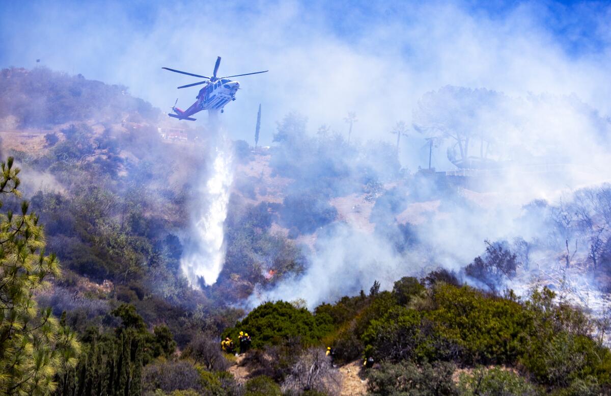 A helicopter drops water on a brush fire.