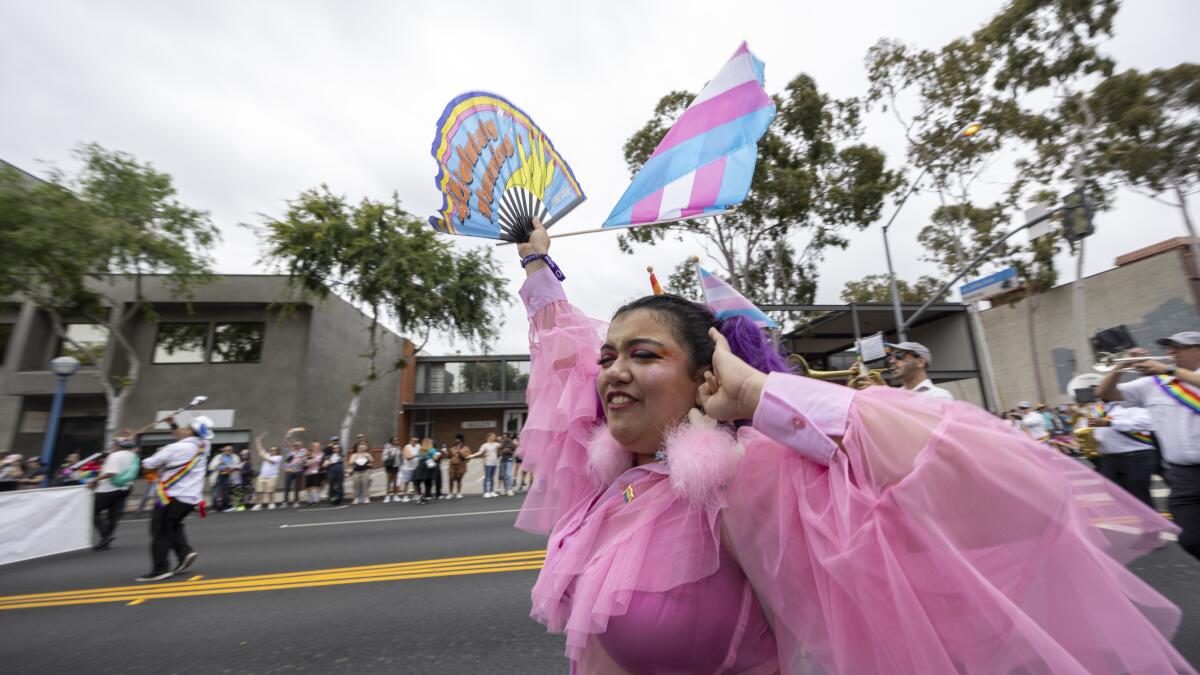A pride marcher waves a fan and a trans pride flag.