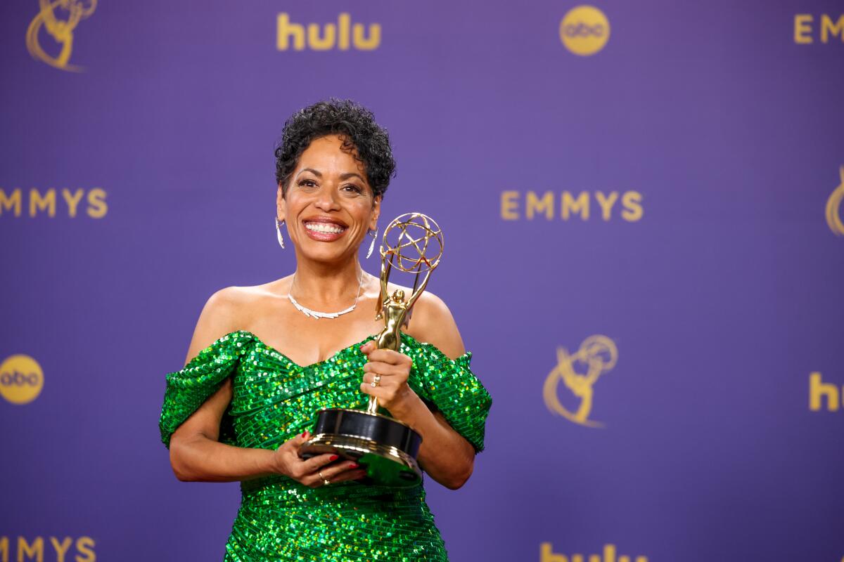 Liza Colon-Zayas, wearing a green dress, smiles and holds an Emmy