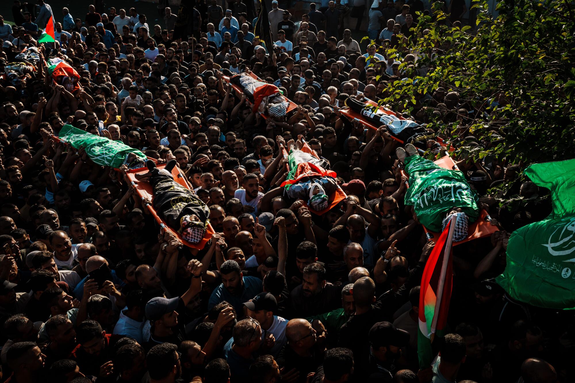 A sea of mourners carry over their heads bodies on litters draped with the Palestinian flag. 