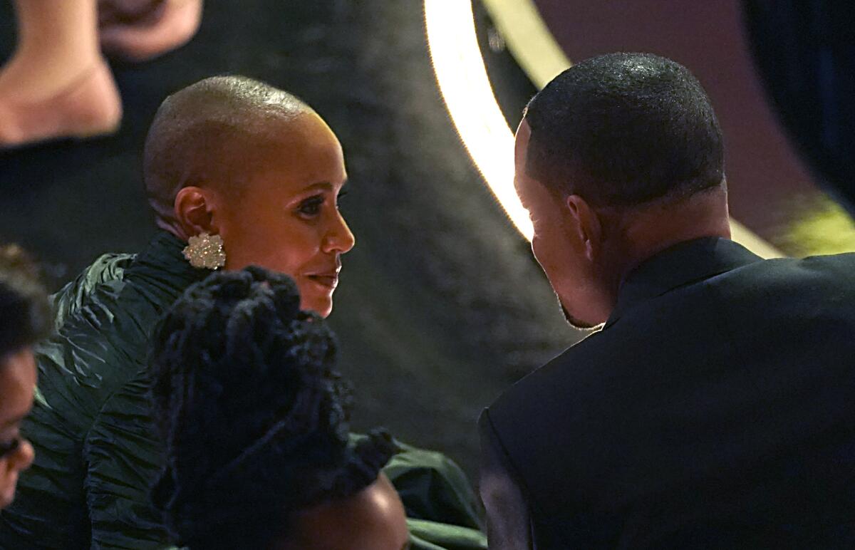 Jada Pinkett Smith is seen in profile while Will Smith is seen from behind as they sit in the audience at the 2022 Oscars.