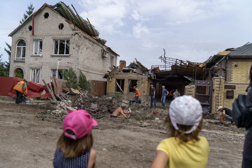Children watch as workers clean up after a rocket strike on a house in Kramatorsk, Donetsk region, eastern Ukraine, Friday, Aug. 12, 2022. There were no injuries reported in the strike. (AP Photo/David Goldman)