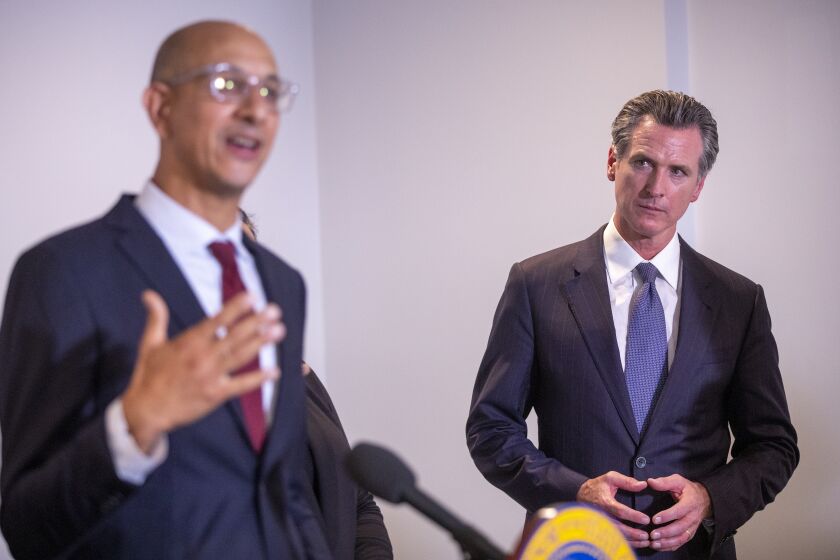 Los Angeles, CA - September 29: Gov. Gavin Newsom, right, listens to Dr. Mark Ghaly, Secretary of Health and Human Services Agency, speak before Newsom signed legislation that supports the state's work to expand mental health services and behavioral health housing as part of a comprehensive approach tackling the homelessness crisis at Alvarado Care Home, a board & care center in Los Angeles on Wednesday, Sept. 29, 2021. (Allen J. Schaben / Los Angeles Times)