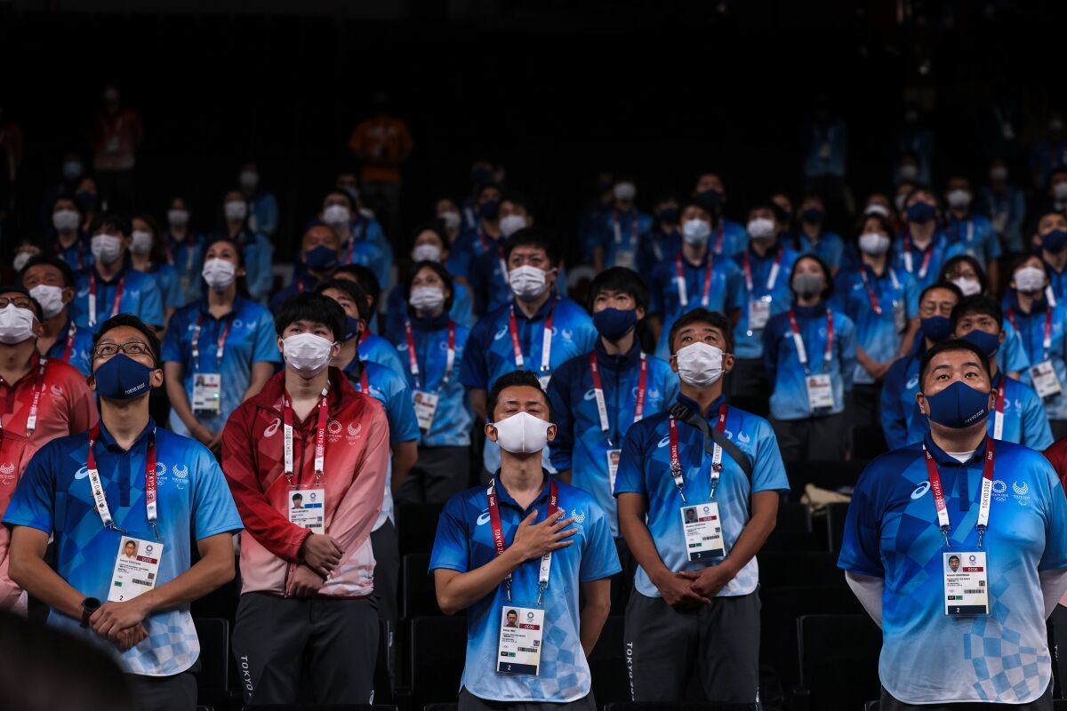 Masked Tokyo Olympics volunteers and staff stand spaced out.