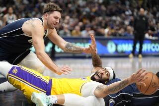 Lakers forward Anthony Davis is sprawled out on the court reaching for a ball while guard Luka Doncic hovers over him 