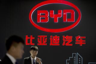 Staff members stand near a logo for the BYD auto company as they wait for visitors at the Beijing International Automotive Exhibition in Beijing, Monday, April 25, 2016. (AP Photo/Mark Schiefelbein)