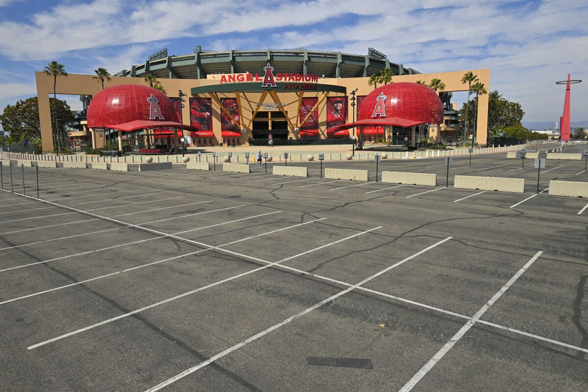 A parking lot is empty as people walk by the front of Angel Stadium.