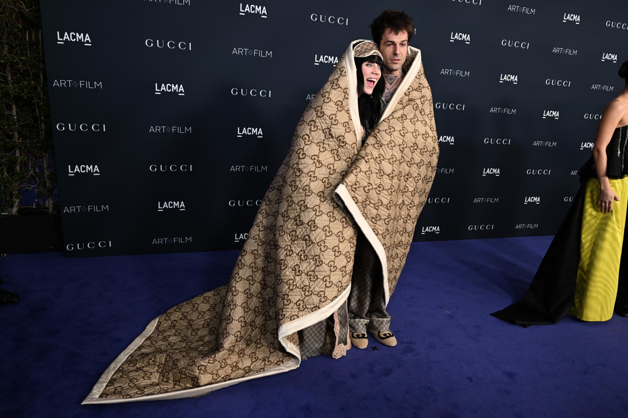 Billie Eilish and Jesse Rutherford wrapped in a blank and pose for a photo.