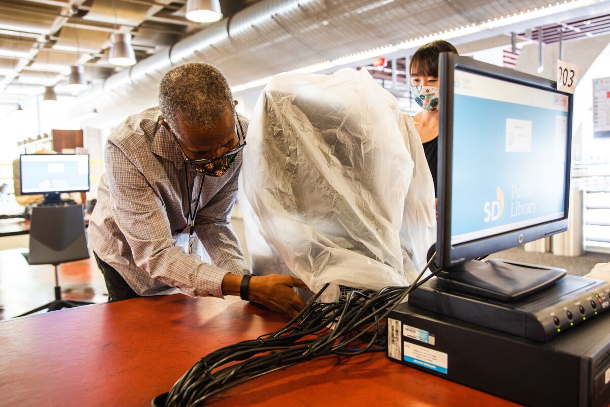 Service area managers Marc Chery and Monnee Tong place a bag over a computer for social distancing.