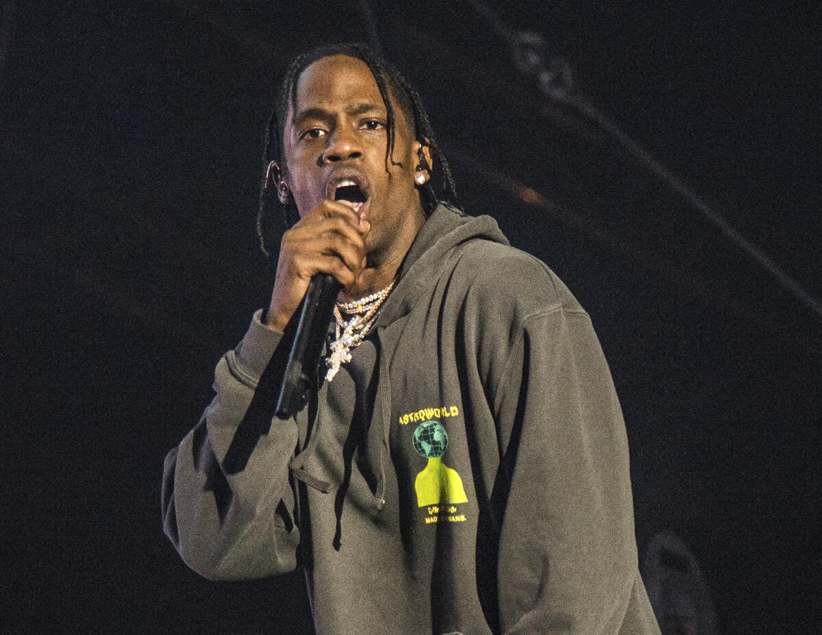 Travis Scott performs in concert wearing a gray hoodie with a yellow design that reads "Astroworld"