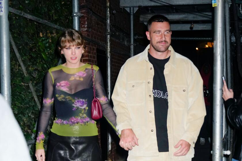  Taylor Swift and Travis Kelce hold hands while walking on a sidewalk