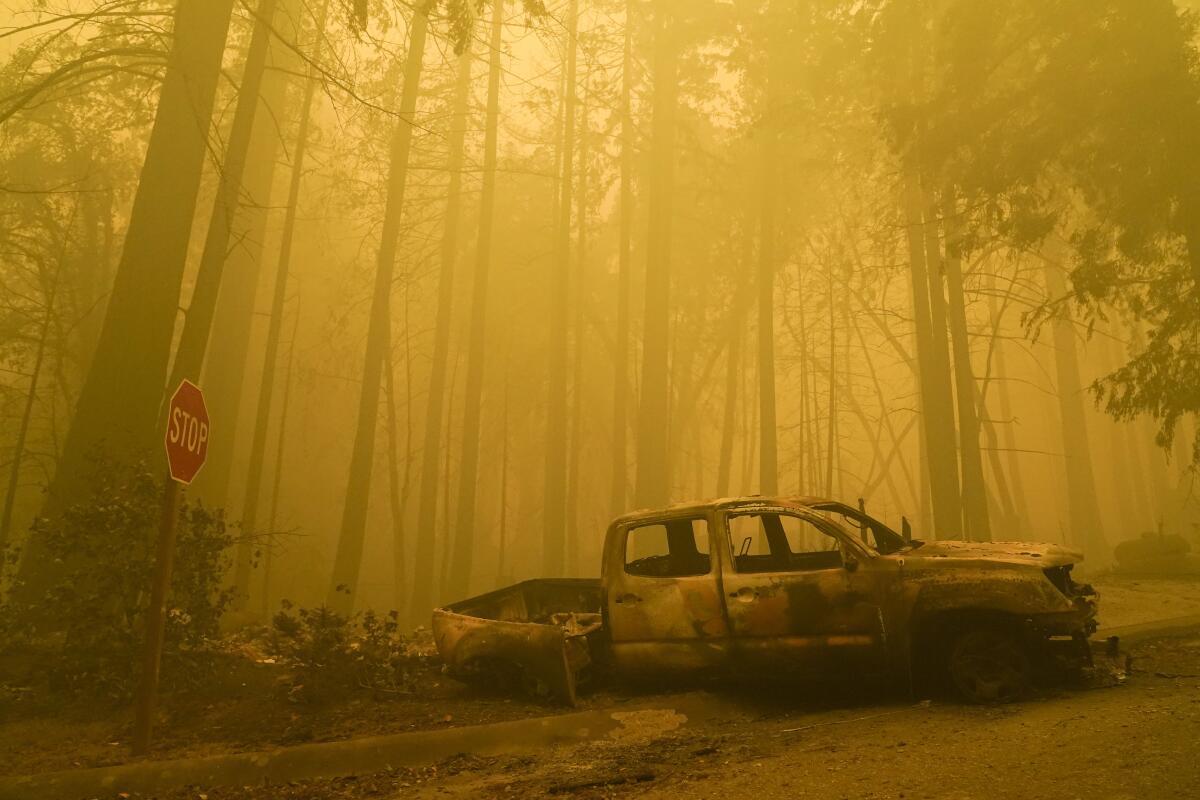 A burned vehicle sits near a fire-ravaged residence in Boulder Creek.