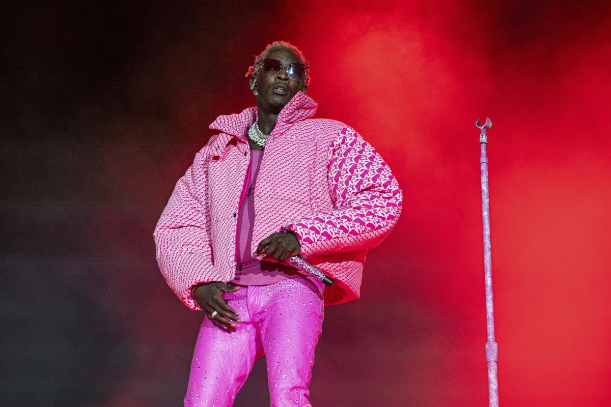 A performer onstage wearing sunglasse, a puffy pink jacket and tight pink pants