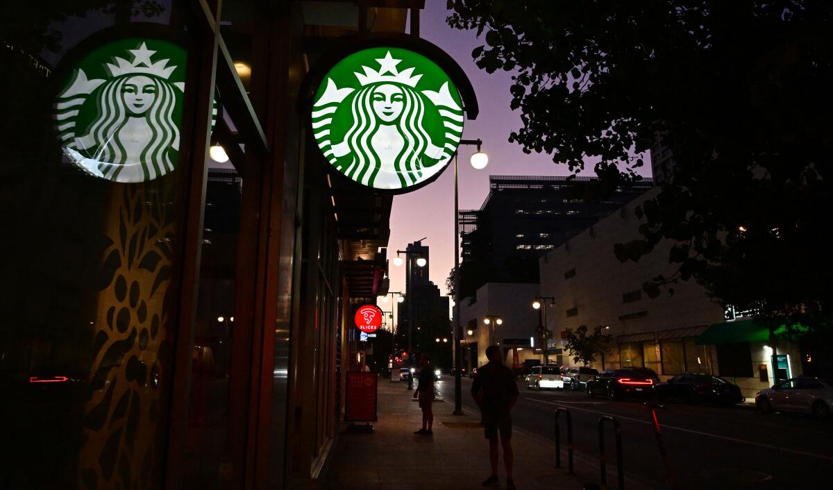 Starbucks' round green mermaid sign shines in the dark outside a closed shop as pedestrians pass by on a city sidewalk