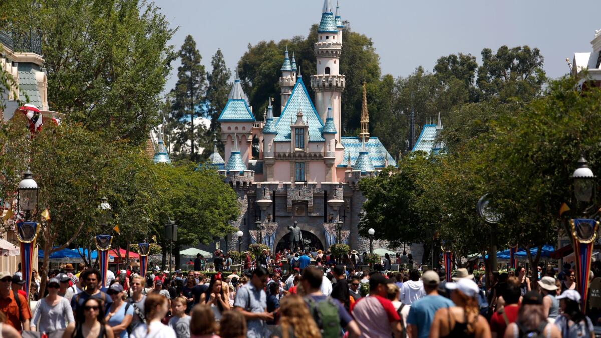Crowds walk down Main Street in front of Sleeping Beauty Castle at Disneyland in Anaheim in June. The park has suspended sales of Southern California annual passes.