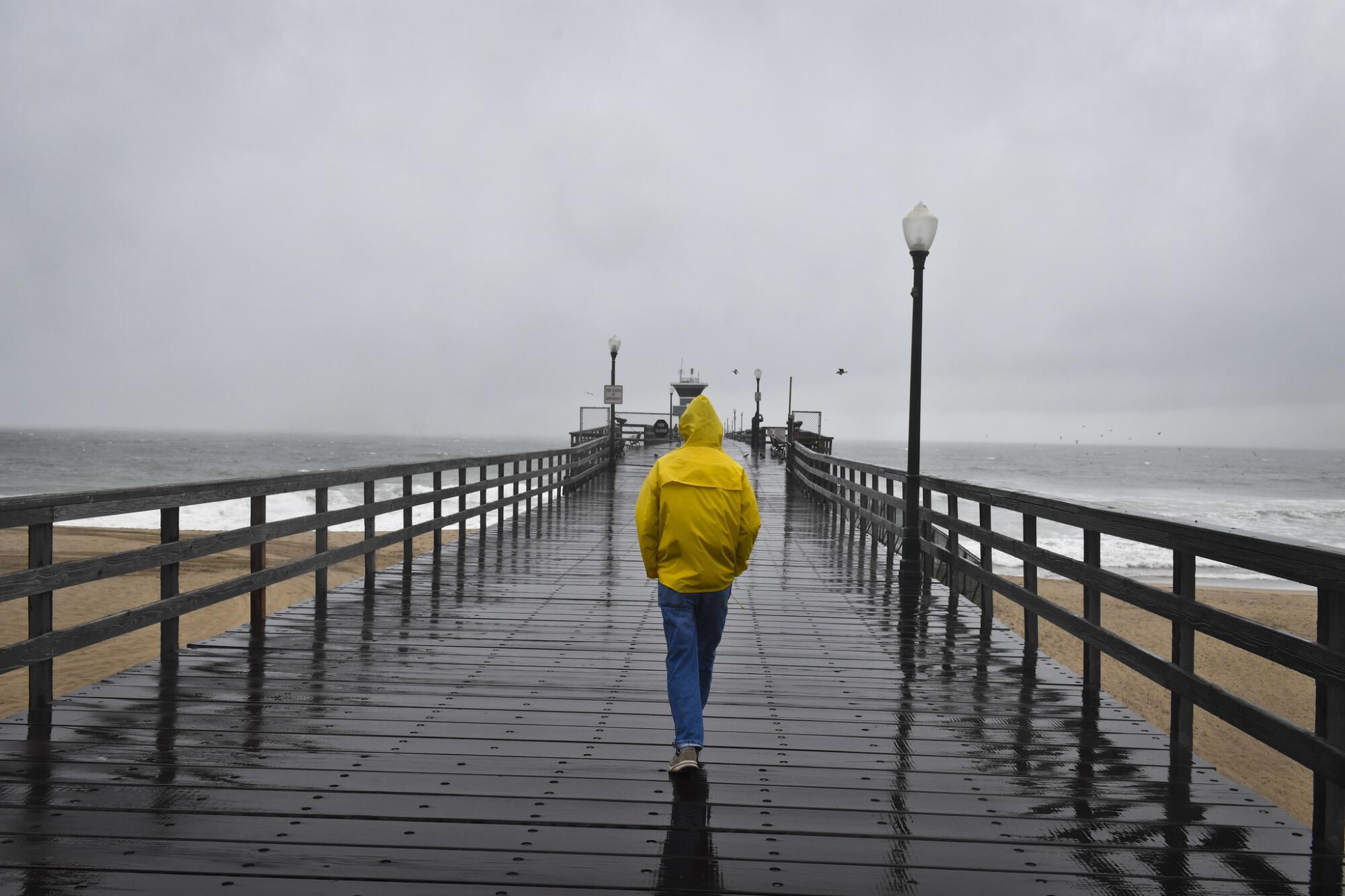 A pedestrian walks along Seal Beach Pier in the rain.