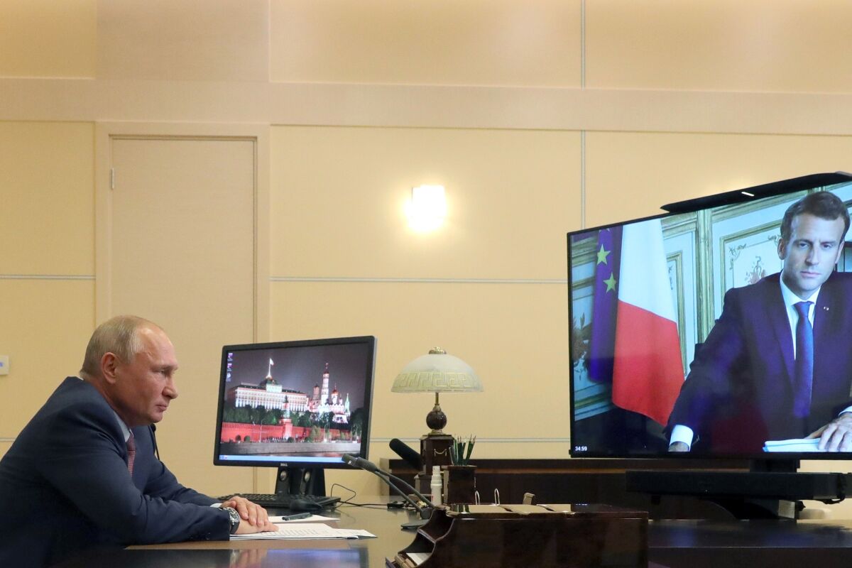 Russian President Vladimir Putin listens to French President Emmanuel Macron, who is shown on a large monitor.