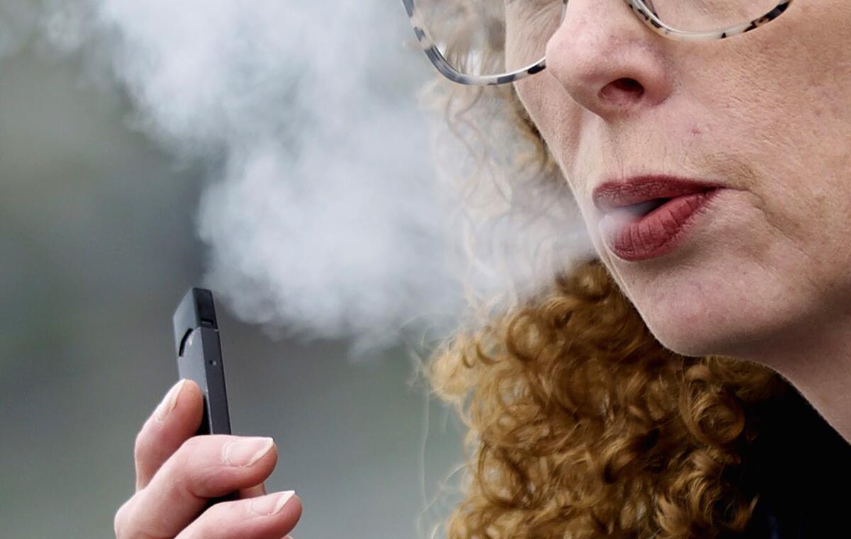  A woman exhales while vaping from a Juul pen e-cigarette