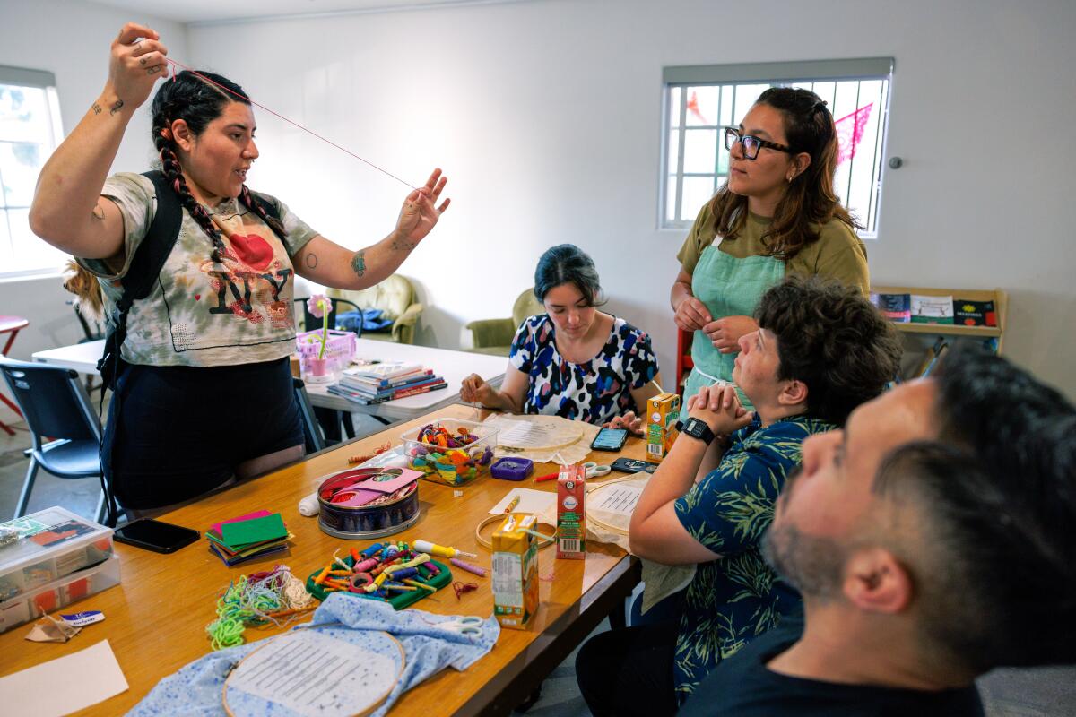 A group of people gathered around a table in a craft room, some holding sewing supplies.