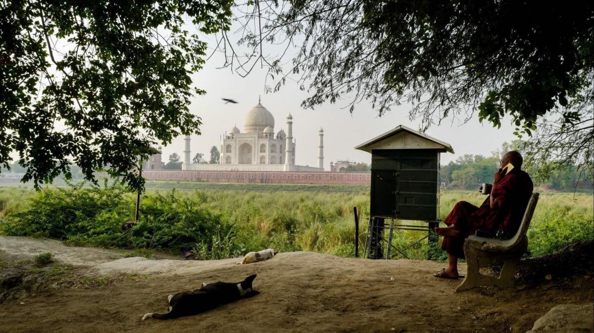 A Buddhist monk converses on the bank of the Yamuna river. From a distance, the Taj Mahal retains its charm.
