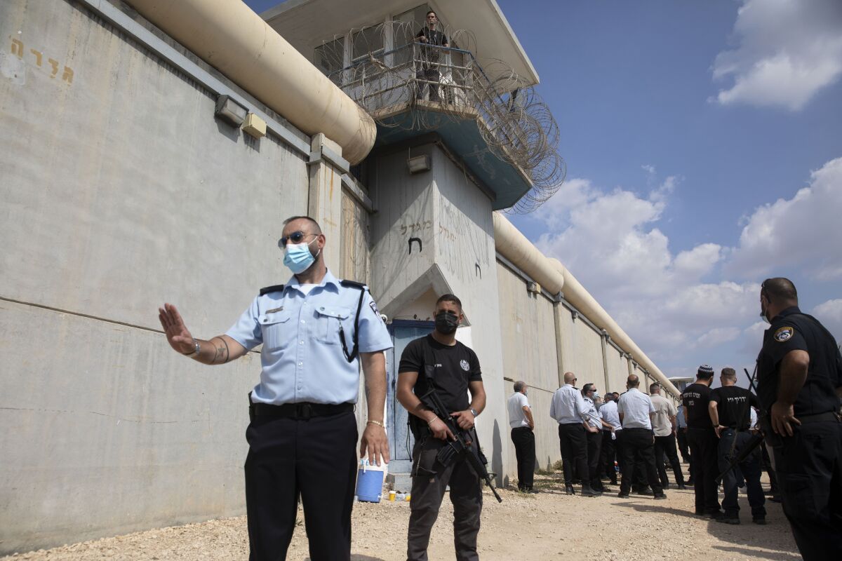 Police officers and prison guards stand outside prison walls.