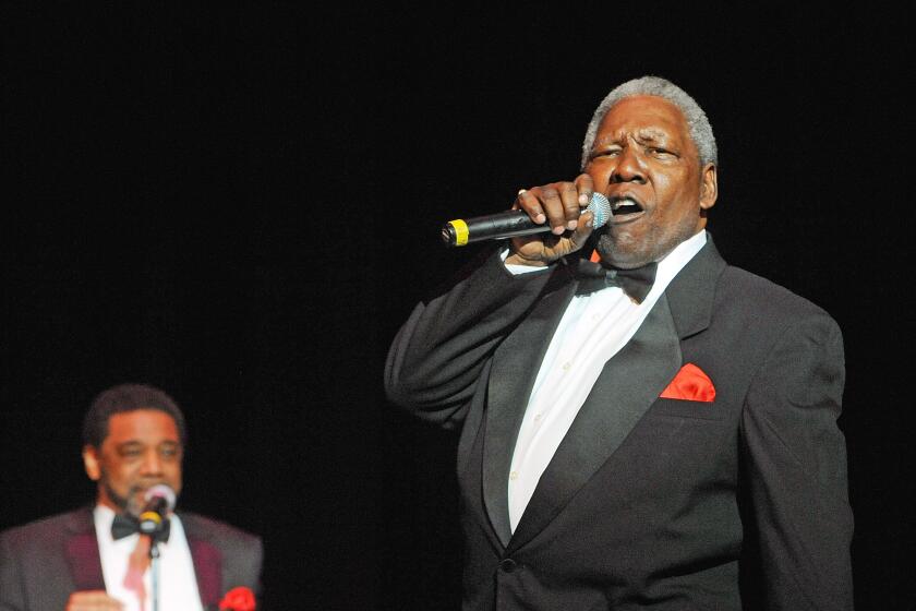 A man with short gray hair wearing a black suit and bowtie and singing into a microphone