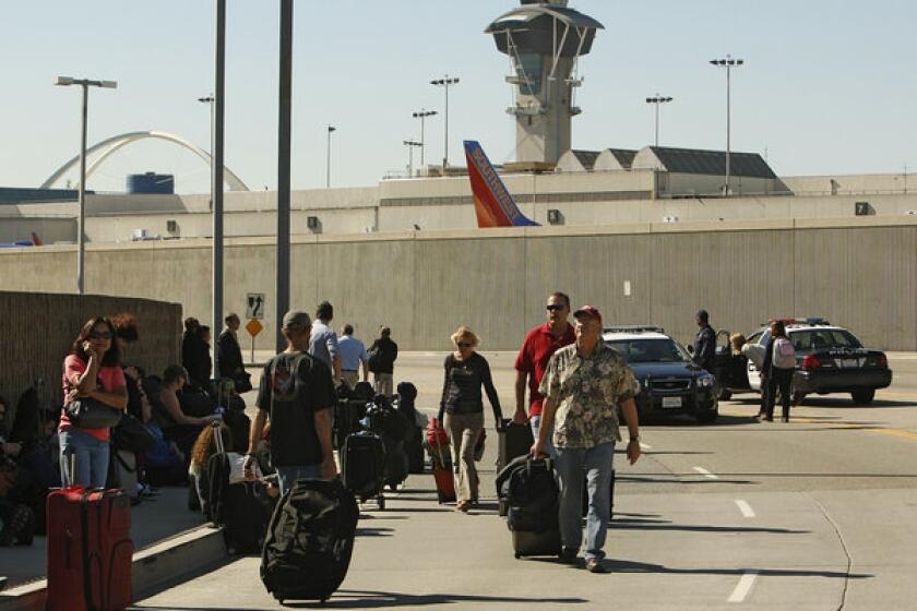 Passengers evacuated from LAX terminals walk with their luggage after a gunman opened fire inside Terminal 3.