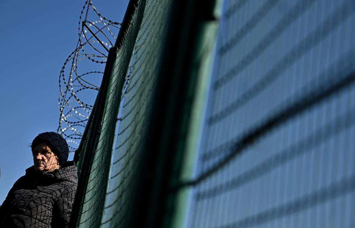 A person waits by a barbed wire fence.