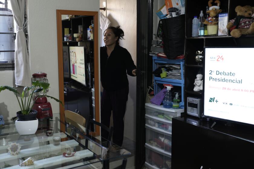 A television program promotes an upcoming presidential debate as domestic worker Concepcion Alejo goes through her morning routine, in her apartment in Mexico City, Wednesday, April 24, 2024. Alejo is among approximately 2.5 million Mexicans — largely women — who serve as domestic workers in the Latin American nation. (AP Photo/Marco Ugarte)