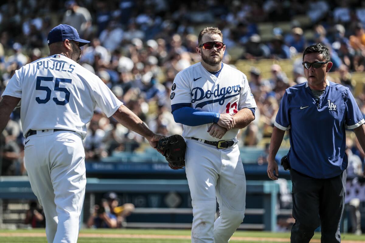 Dodgers first baseman Max Muncy leaves the field with a team trainer as Albert Pujols enters the game.