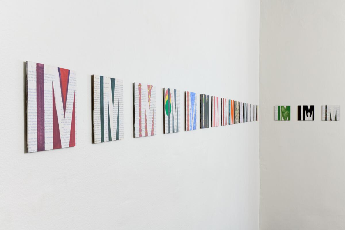 Several pieces of square artwork with the letters "I M" on a wall.