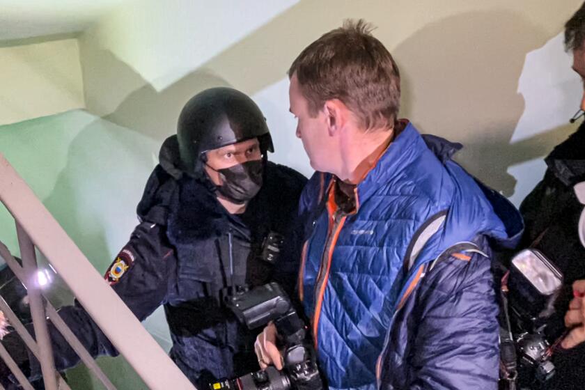 A police officer pushes photographers from a door of the apartment where Oleg Navalny, brother of jailed opposition leader Alexei Navalny lives in Moscow, Russia, Wednesday, Jan. 27, 2021. Police are searching the Moscow apartment of jailed Russian opposition leader Alexei Navalny, another apartment where his wife is living and two offices of his anti-corruption organization. Navalny's aides reported the Wednesday raids on social media. (AP Photo/Mstyslav Chernov)