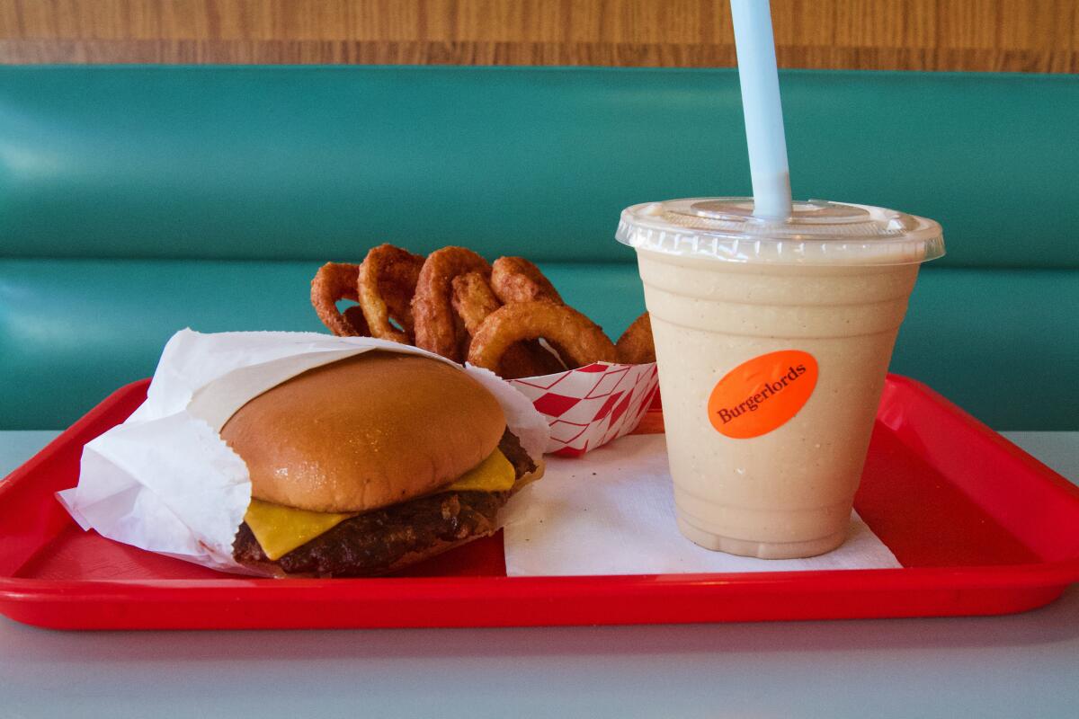 A spread from Burgerlords on a red tray against a green booth: Oklahoma-style burger, onion rings and a tahini milkshake.