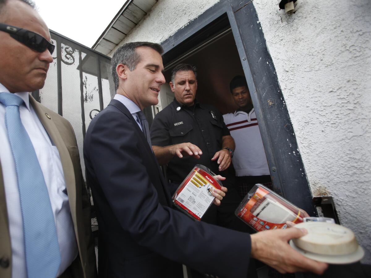 Los Angeles mayor Eric Garcetti hands off an old smoke detector being replaced by a new "First Alert" smoke detector to resident on 39th Place in South LA on Monday, where city officials announced a new initiative aimed at reducing residential fires.