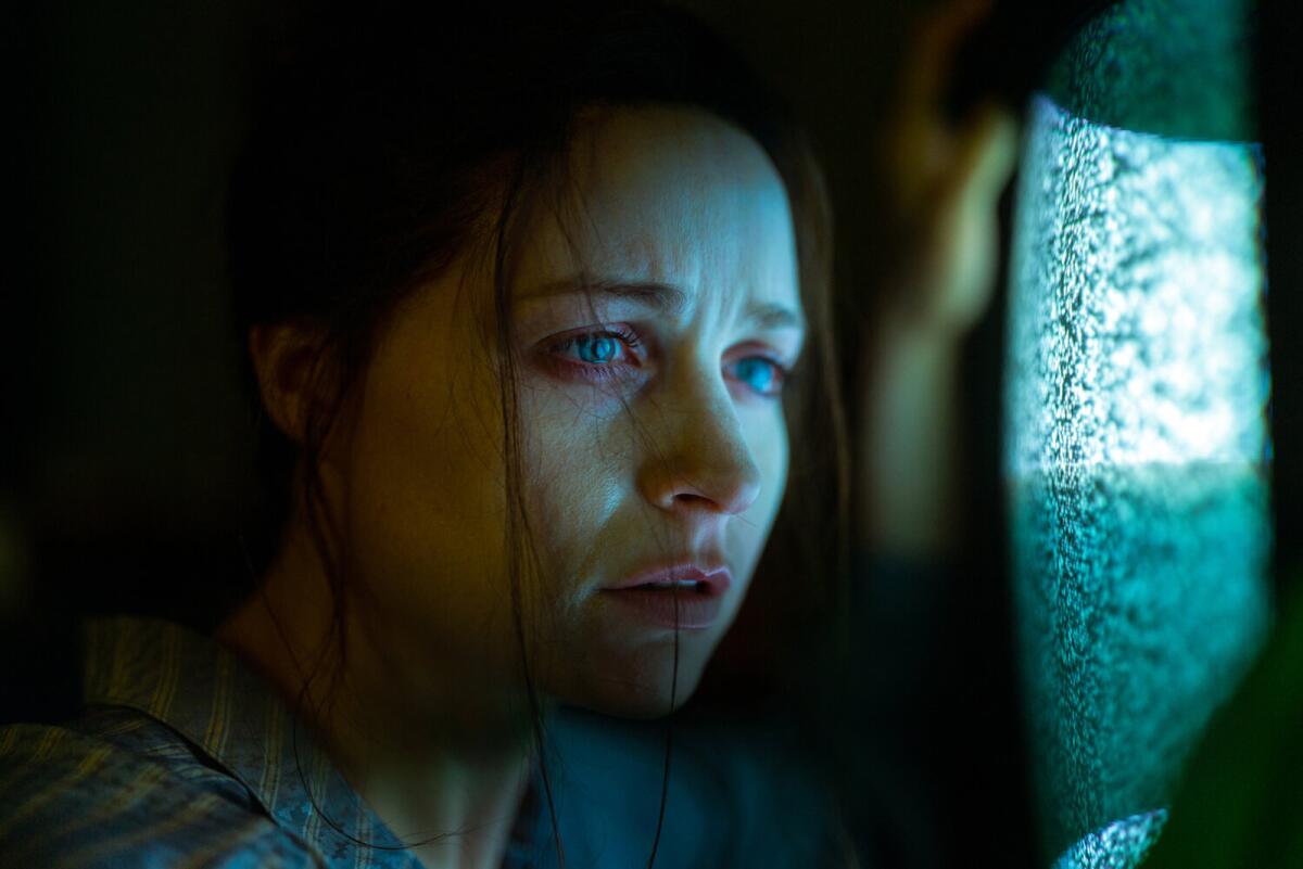 A young woman peers ominously out a window in the movie "Censor."