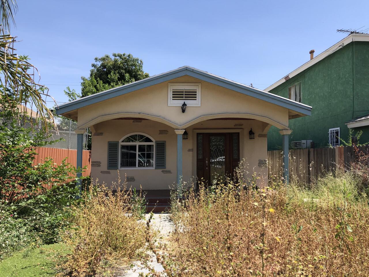 A rundown house before it was remodeled, with overgrown weeds in the front yard. 