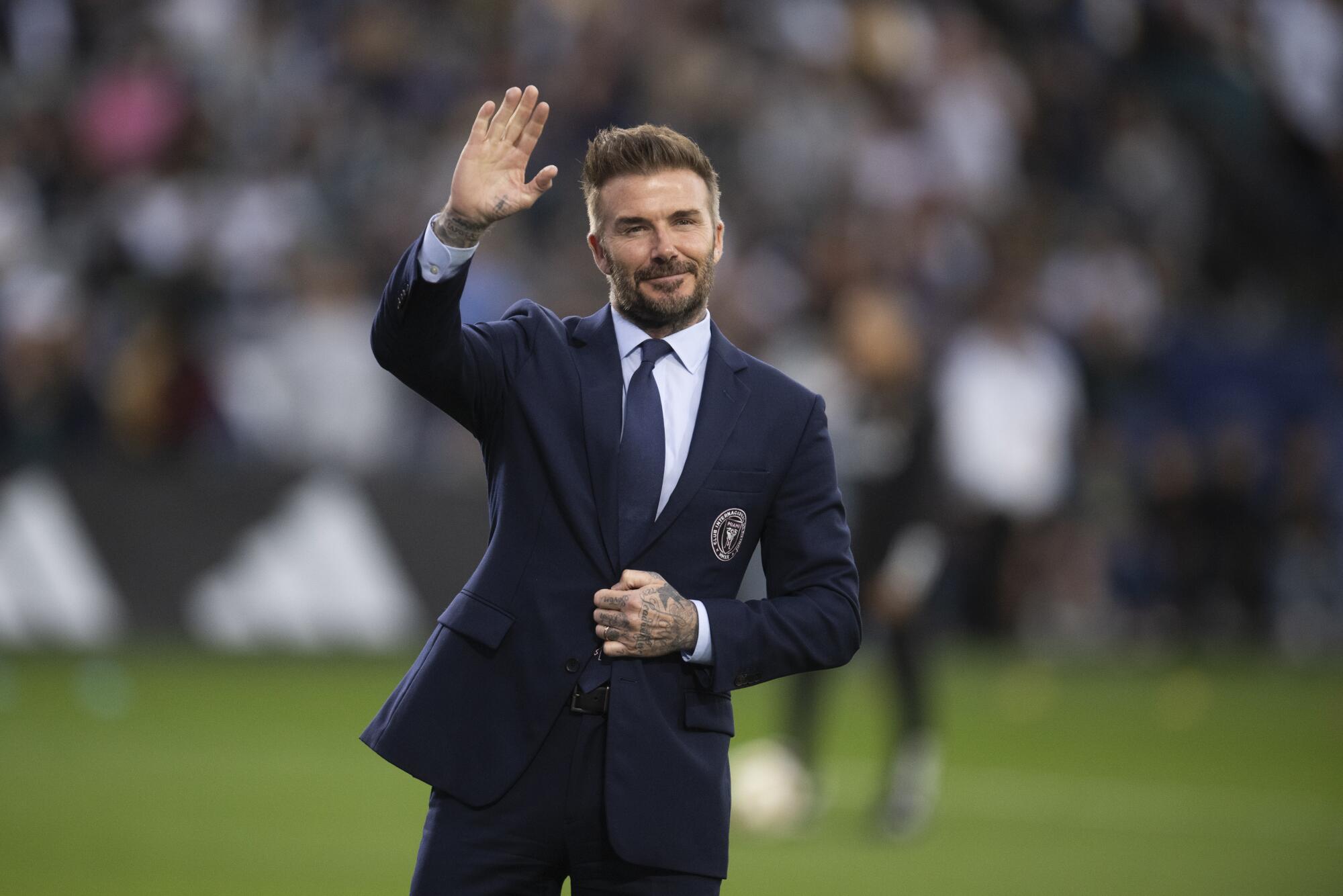 David Beckham wears a suit and waves to the stands.