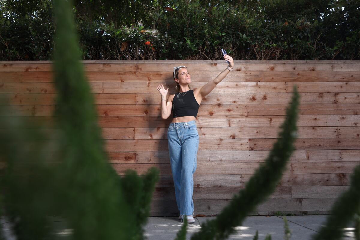 A woman in a dark cropped top and jeans makes gestures with her hands against a wooden backdrop.